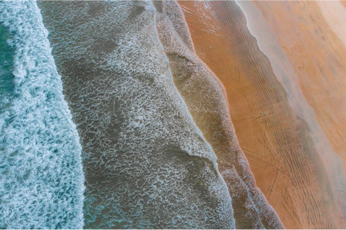 Aerial view of ocean waves washing onto a sandy beach in a diagonal abstract composition