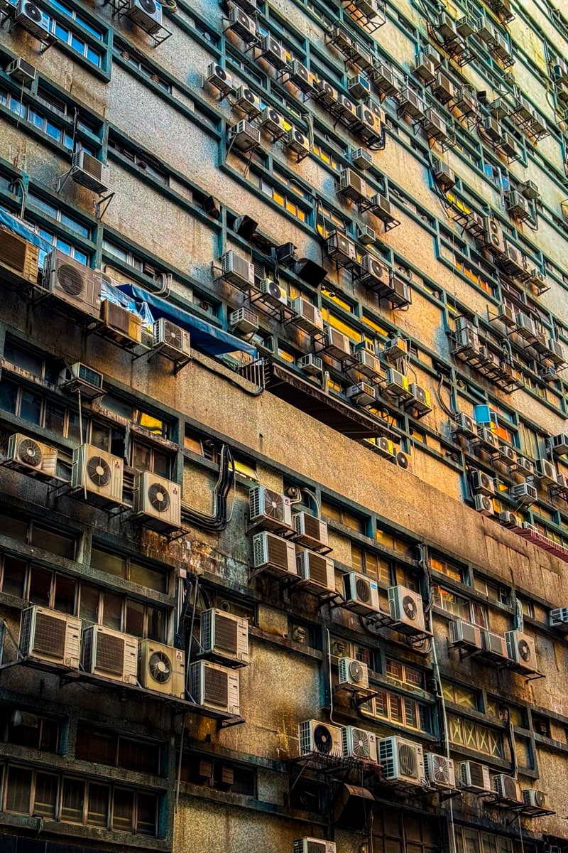 Weathered building facade covered in air-conditioning units and laundry lines in warm light