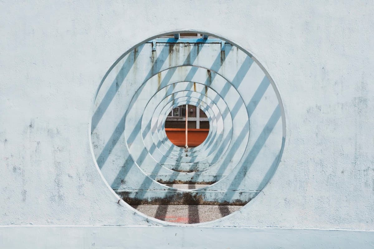 Concentric circular metal rings in a white concrete wall creating a geometric tunnel pattern