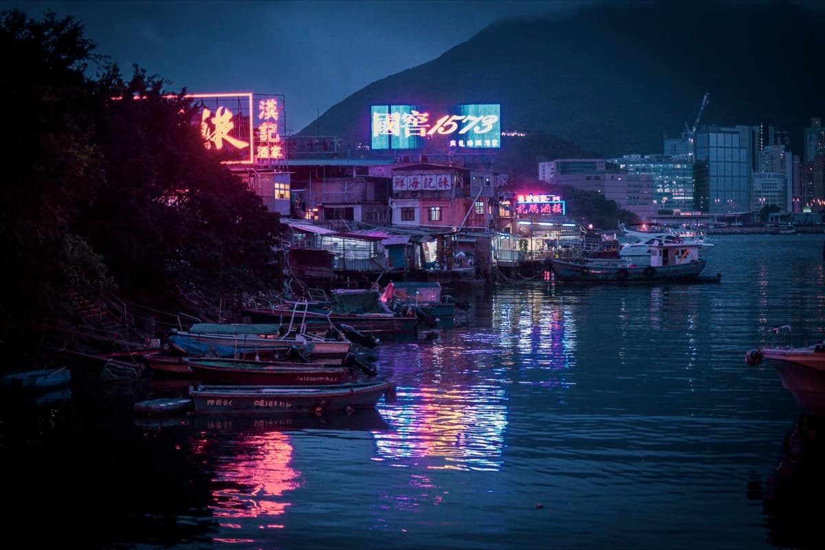 Fishing village harbour at night with neon signs reflecting on calm water and moored boats
