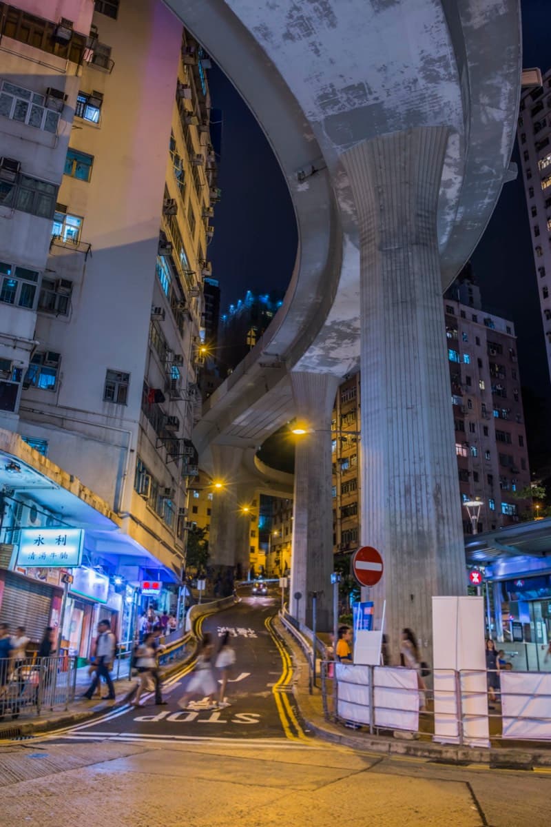 Curved highway flyover at night between residential buildings with pedestrians below