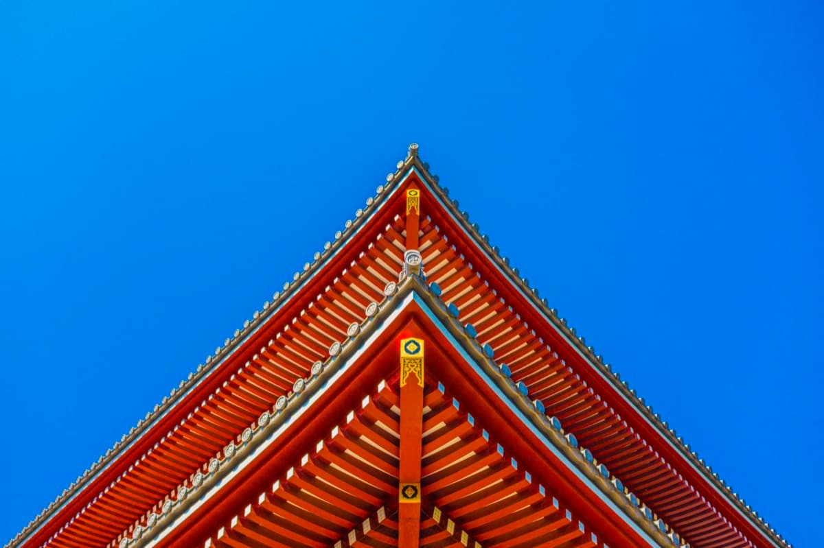 Japanese pagoda rooftop with ornate wooden rafters and gold details against blue sky