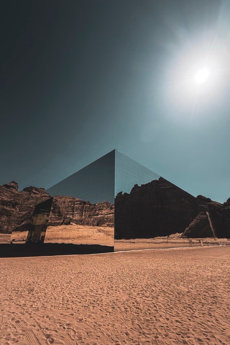 Large mirrored Maraya Concert Hall reflecting desert cliffs under a hazy sun