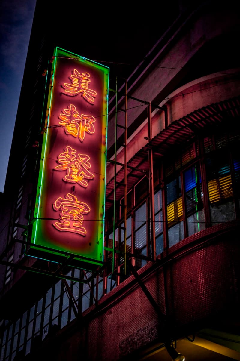 Neon sign reading Mido Cafe in orange and green mounted on an old building at night