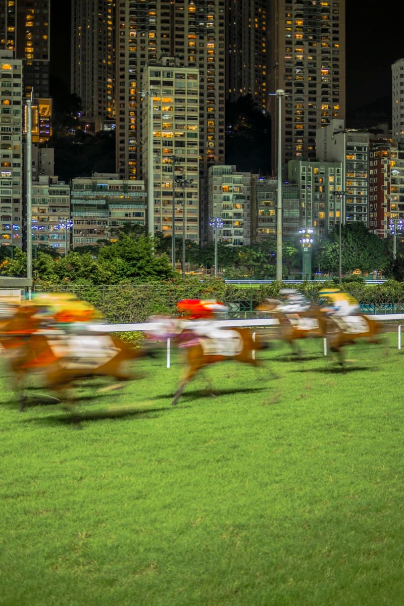 Horse racing at night at Happy Valley Racecourse with illuminated high-rises behind