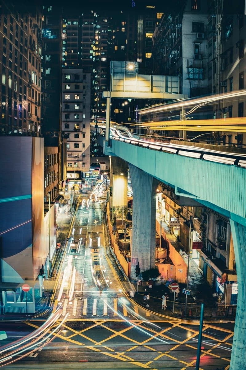 Long-exposure night shot of light trails from traffic under an elevated walkway in Sheung Wan
