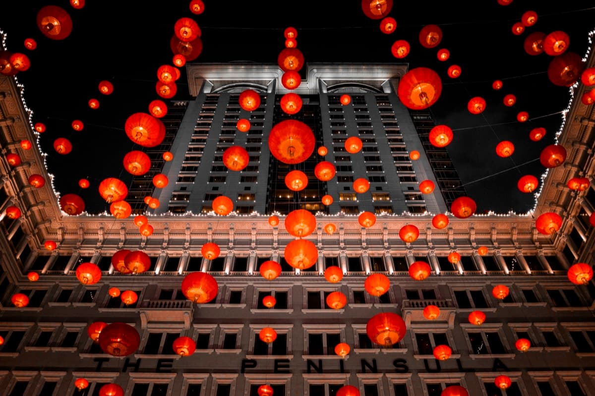 The Peninsula Hotel facade at night viewed through a canopy of glowing red lanterns