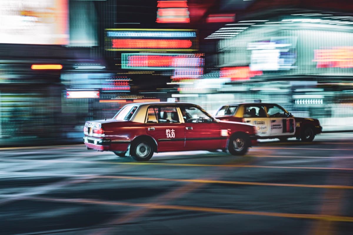 Red Hong Kong taxi speeding through neon-lit streets with motion blur