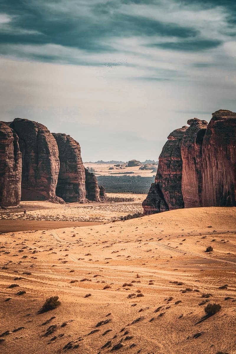 Towering sandstone rock formations flanking a sandy valley passage in the desert