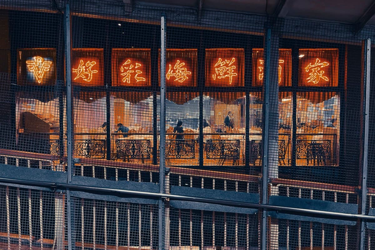 Seafood restaurant neon sign viewed through scaffolding mesh with diners inside