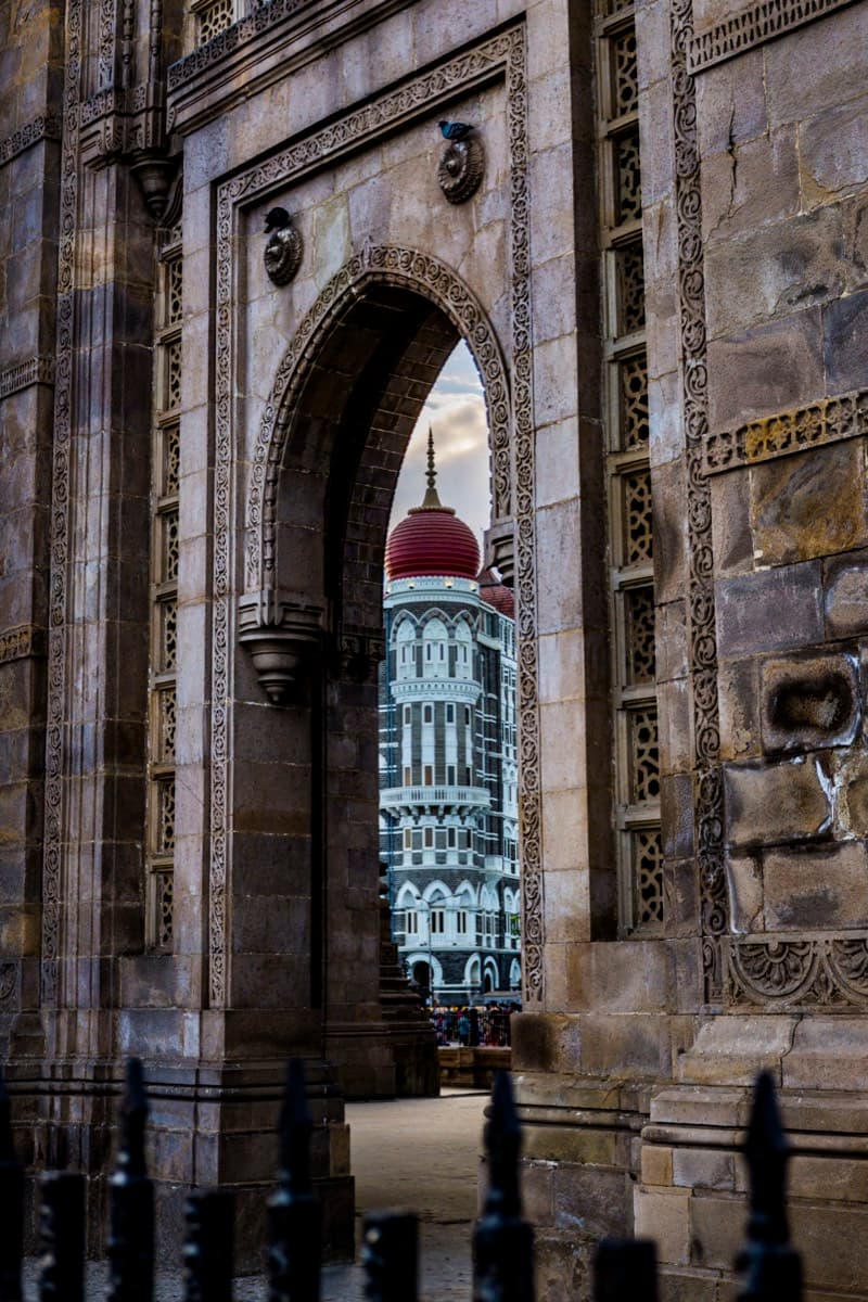 Taj Mahal Palace Hotel facade framed through the Gateway of India stone archway