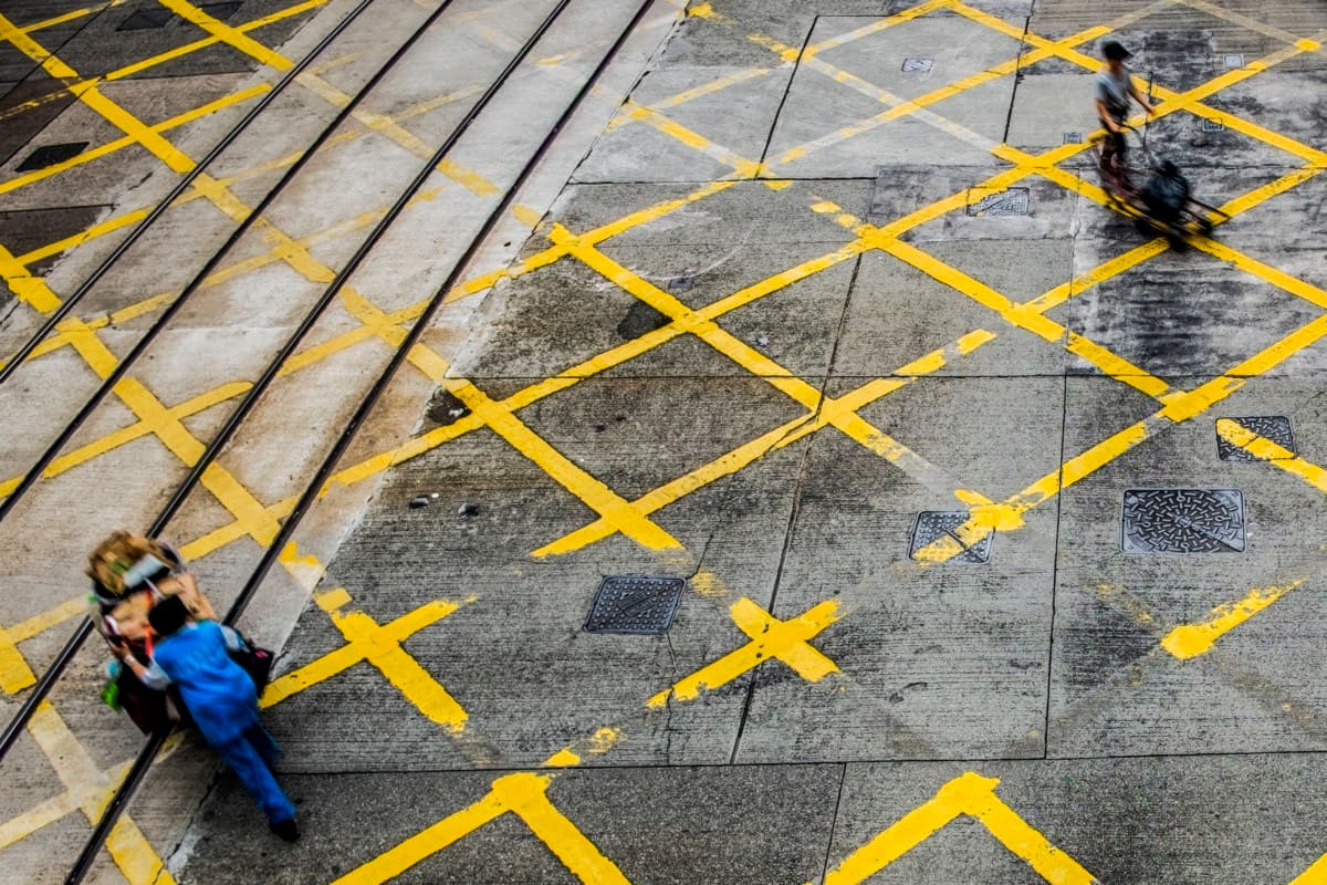 Aerial view of pedestrians crossing yellow road markings and tram tracks on Des Voeux Road Central